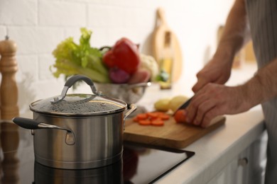 Photo of Homemade bouillon recipe. Man cutting carrot in kitchen, focus on pot