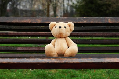 Lonely teddy bear on wooden bench outdoors