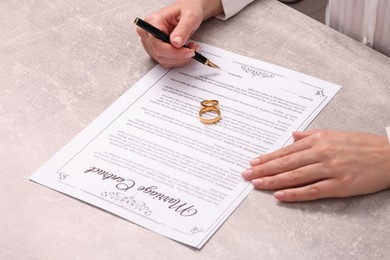 Woman signing marriage contract at light grey table, closeup