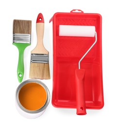 Photo of Can of orange paint, roller, container and brushes on white background, top view