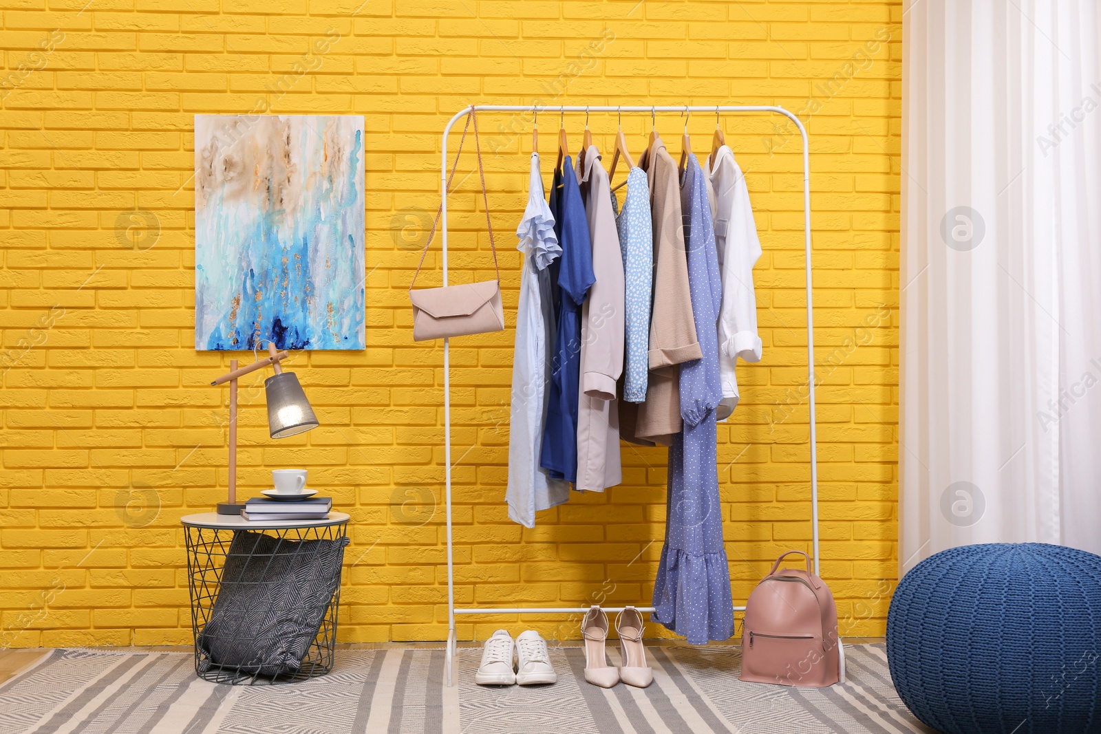 Photo of Rack with different stylish clothes and shoes near yellow brick wall in room