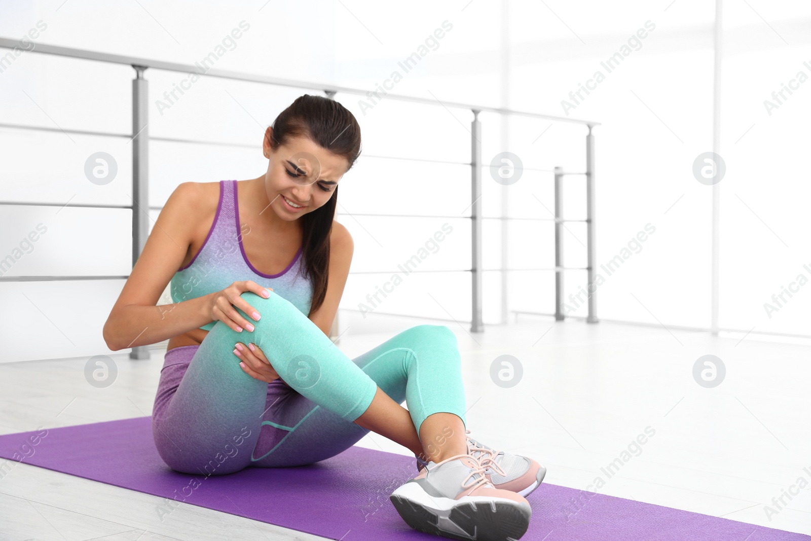 Photo of Young woman in sportswear having knee problems at gym. Space for text