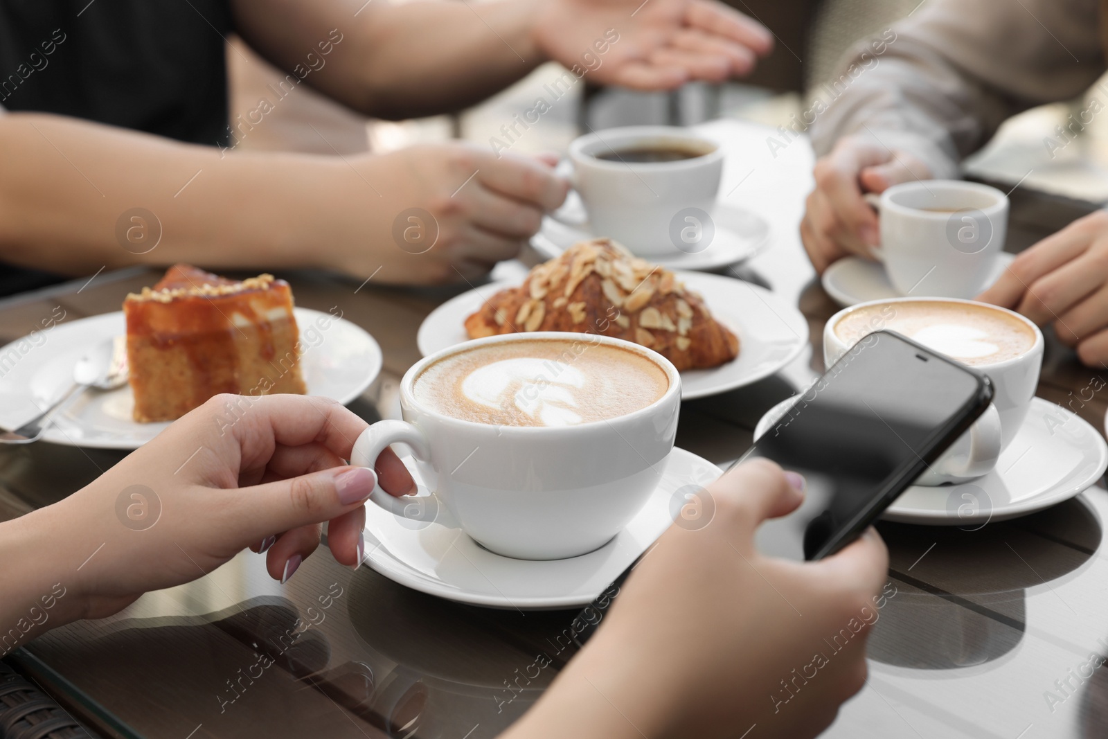 Photo of Friends drinking coffee at wooden table in outdoor cafe, closeup