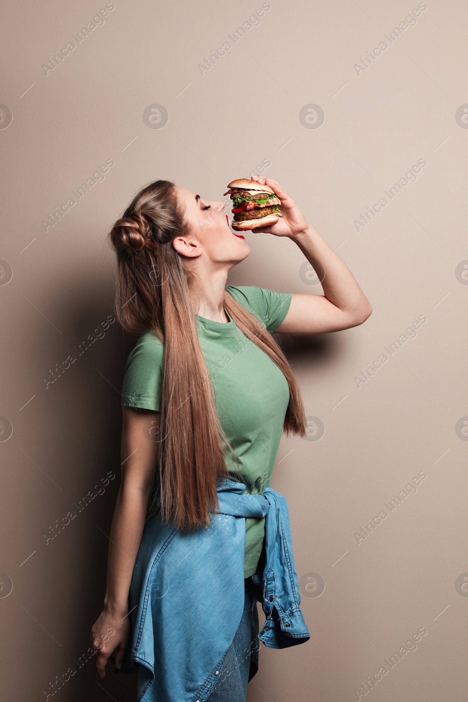 Photo of Pretty woman eating tasty burger on color background. Space for text