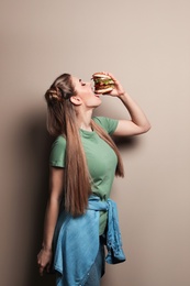 Pretty woman eating tasty burger on color background. Space for text