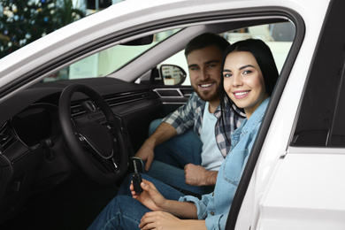 Happy couple with car key sitting in modern auto at dealership