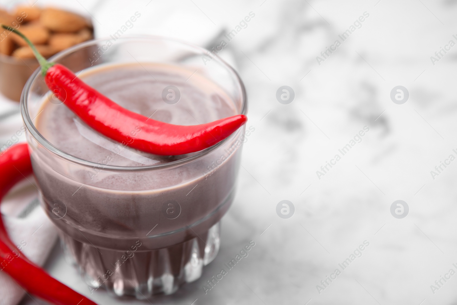 Photo of Glass of hot chocolate with chili pepper on white marble table, closeup. Space for text