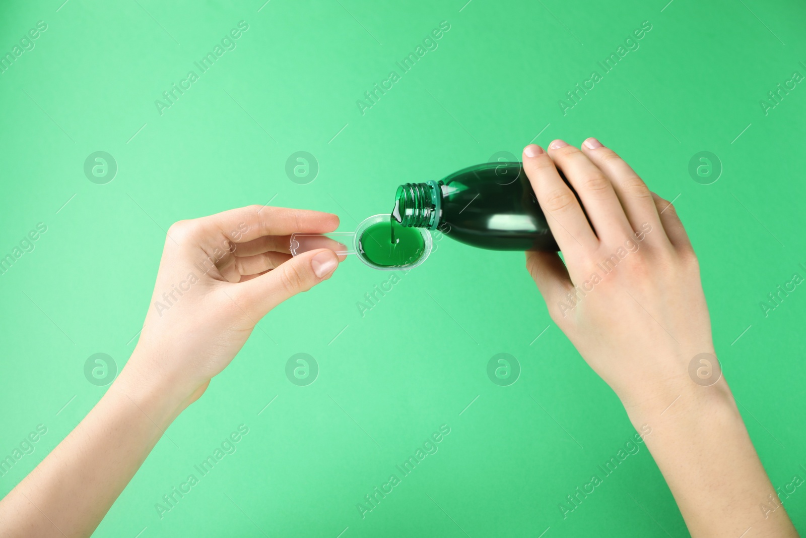 Photo of Woman pouring cough syrup into dosing spoon on green background, closeup