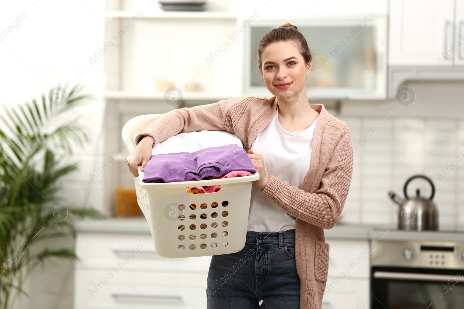Photo of Woman holding basket with clean laundry in kitchen