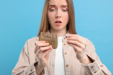 Woman untangling her lost hair from comb on light blue background, selective focus. Alopecia problem