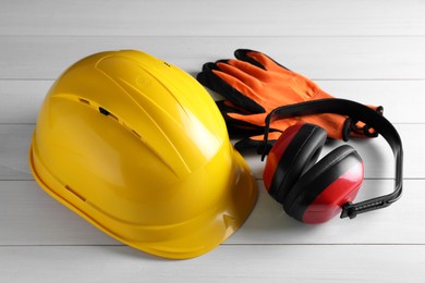 Photo of Hard hat, earmuffs and gloves on white wooden table. Safety equipment