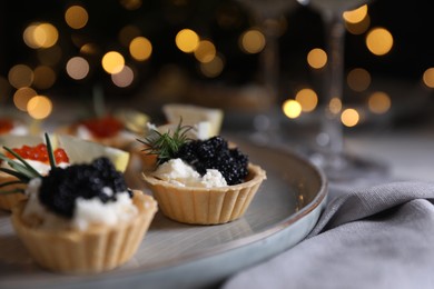 Photo of Delicious tartlets with red and black caviar served on white wooden table against blurred festive lights, closeup. Space for text