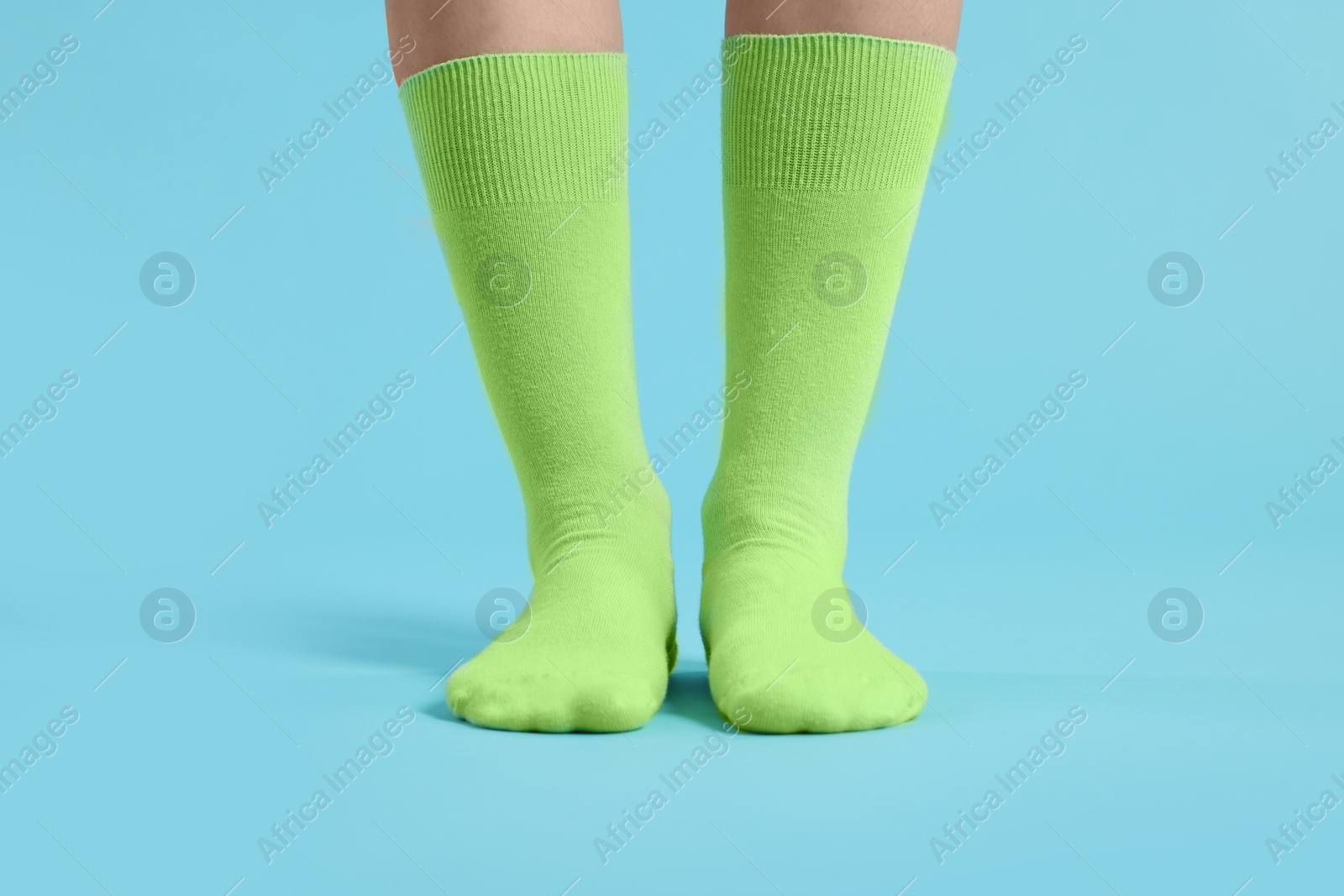 Photo of Woman in stylish lime socks on light blue background, closeup