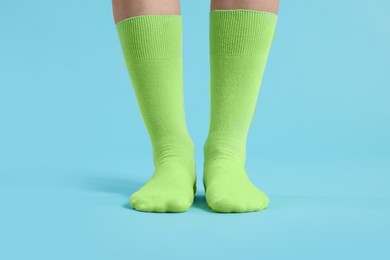 Woman in stylish lime socks on light blue background, closeup