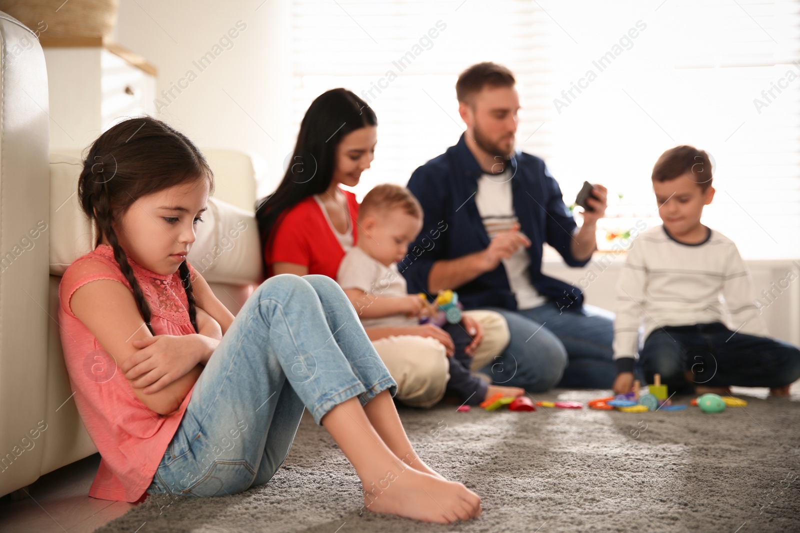 Photo of Unhappy little girl feeling jealous while parents spending time with other children at home