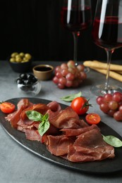Delicious bresaola, tomato and basil leaves on grey textured table