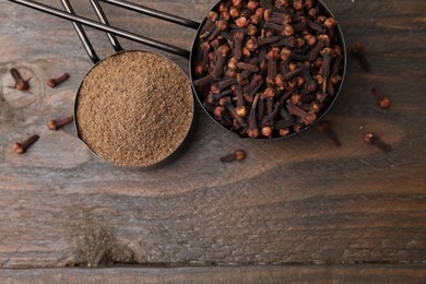 Aromatic clove powder and dried buds in scoops on wooden table, top view. Space for text