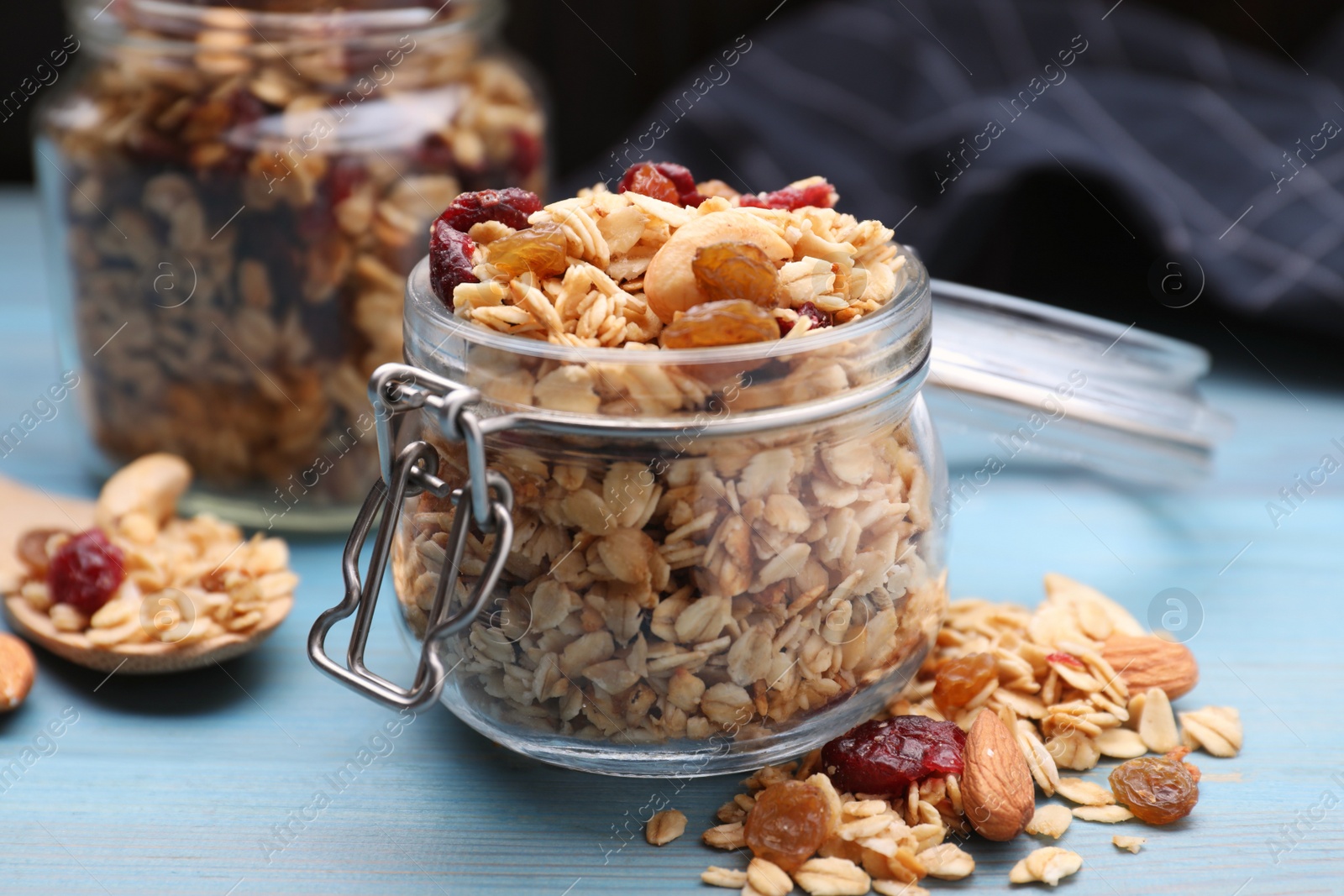 Photo of Jars of tasty granola with nuts and dry fruits on light blue wooden table, closeup