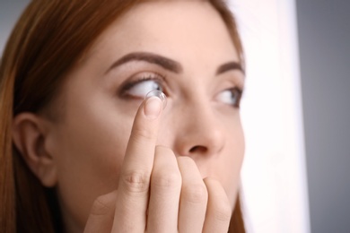 Young woman putting contact lens in her eye, closeup