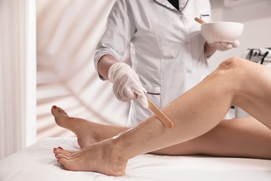 Photo of Professional cosmetologist applying gel on client's leg before laser epilation procedure in salon, closeup