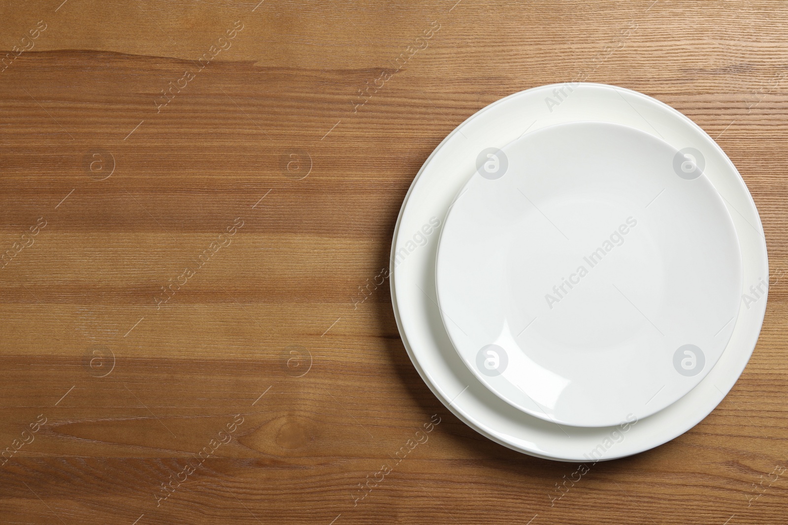 Photo of Empty ceramic plates on wooden table, top view. Space for text