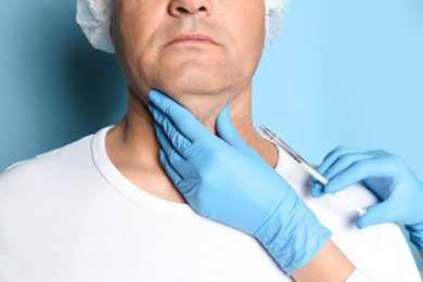 Photo of Mature man with double chin receiving injection on blue background, closeup