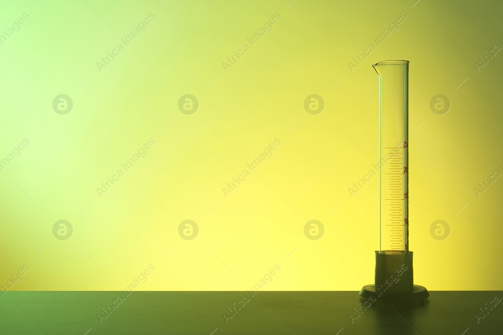 Photo of Empty graduated cylinder on table against color background. Chemistry laboratory glassware