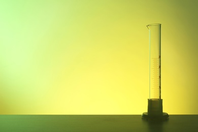 Photo of Empty graduated cylinder on table against color background. Chemistry laboratory glassware