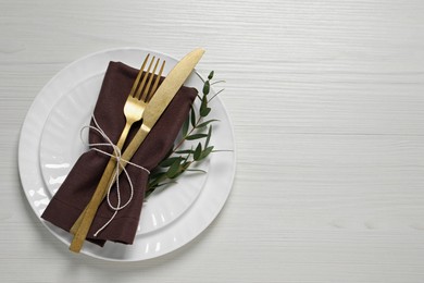 Stylish setting with cutlery and eucalyptus leaves on white wooden table, top view. Space for text