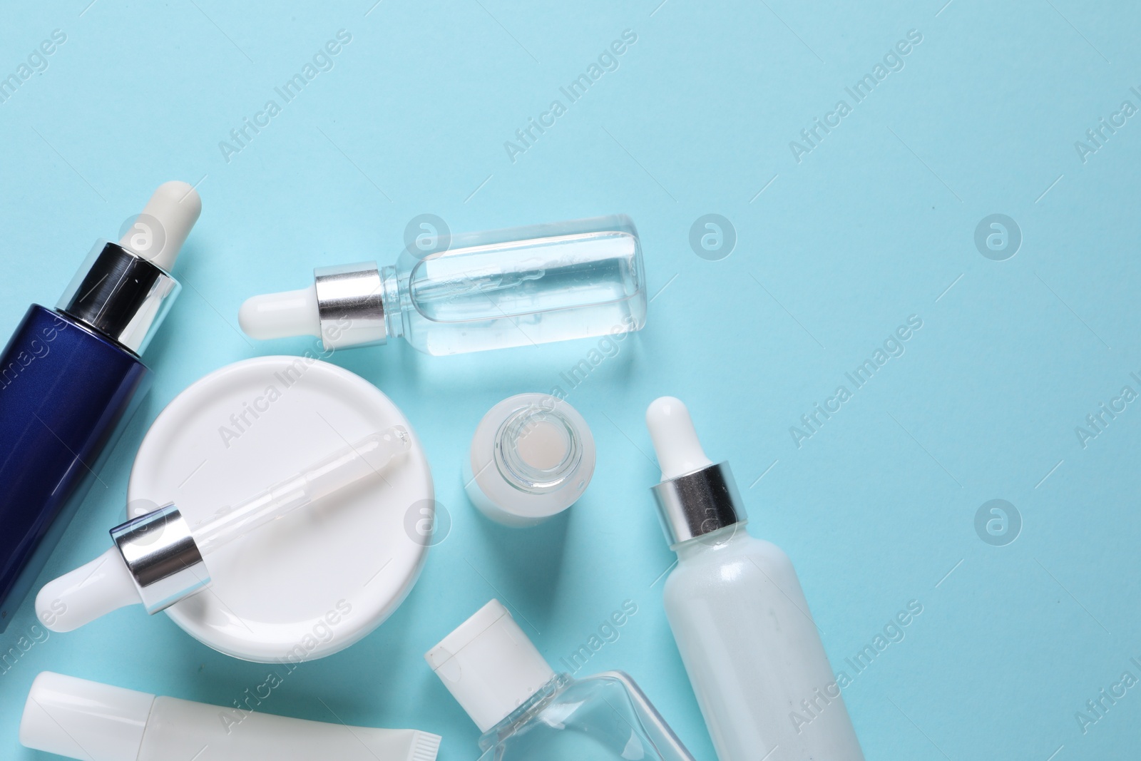 Photo of Many bottles and tube of cosmetic serum on light blue background, flat lay. Space for text