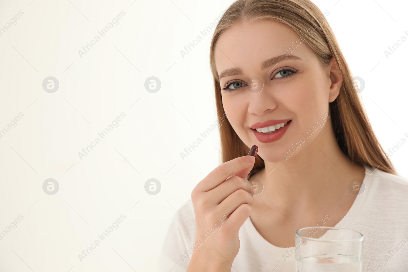 Photo of Young woman with glass of water taking vitamin capsule on light background. Space for text