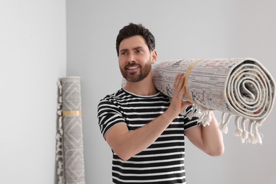Smiling man holding rolled carpet in room