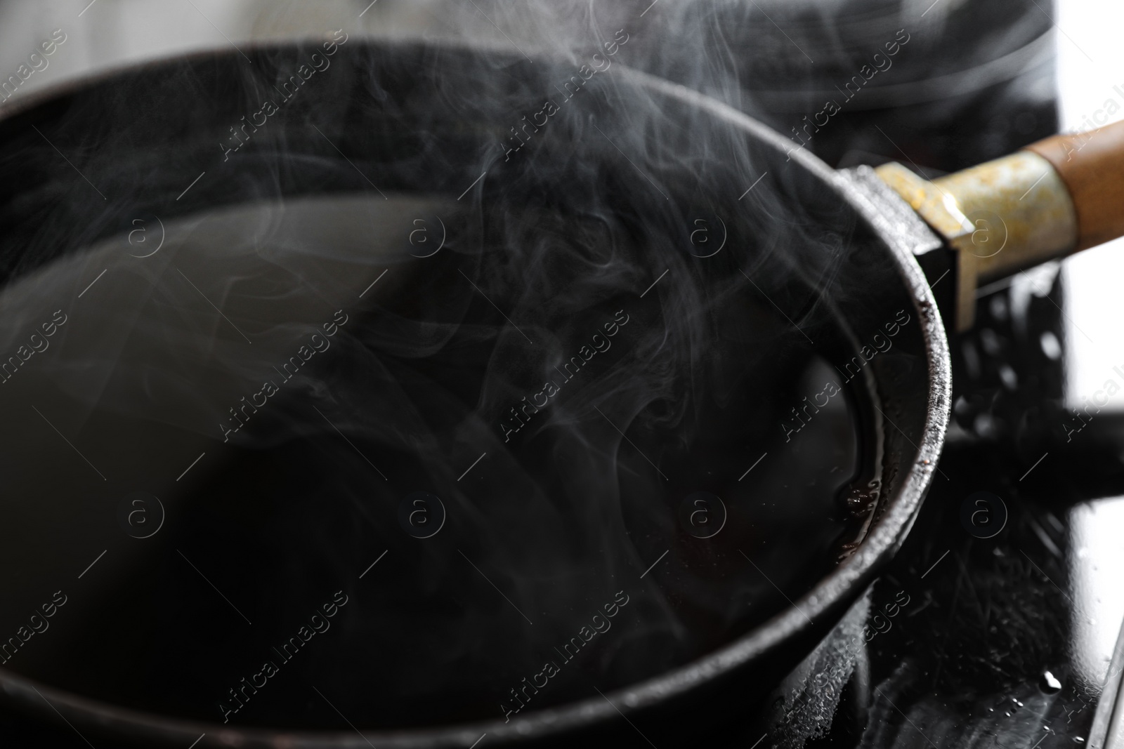 Photo of Frying pan with hot used cooking oil on stove, closeup