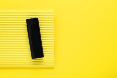 Photo of Stylish small pocket lighter with corrugated fiberboard on yellow background, top view. Space for text