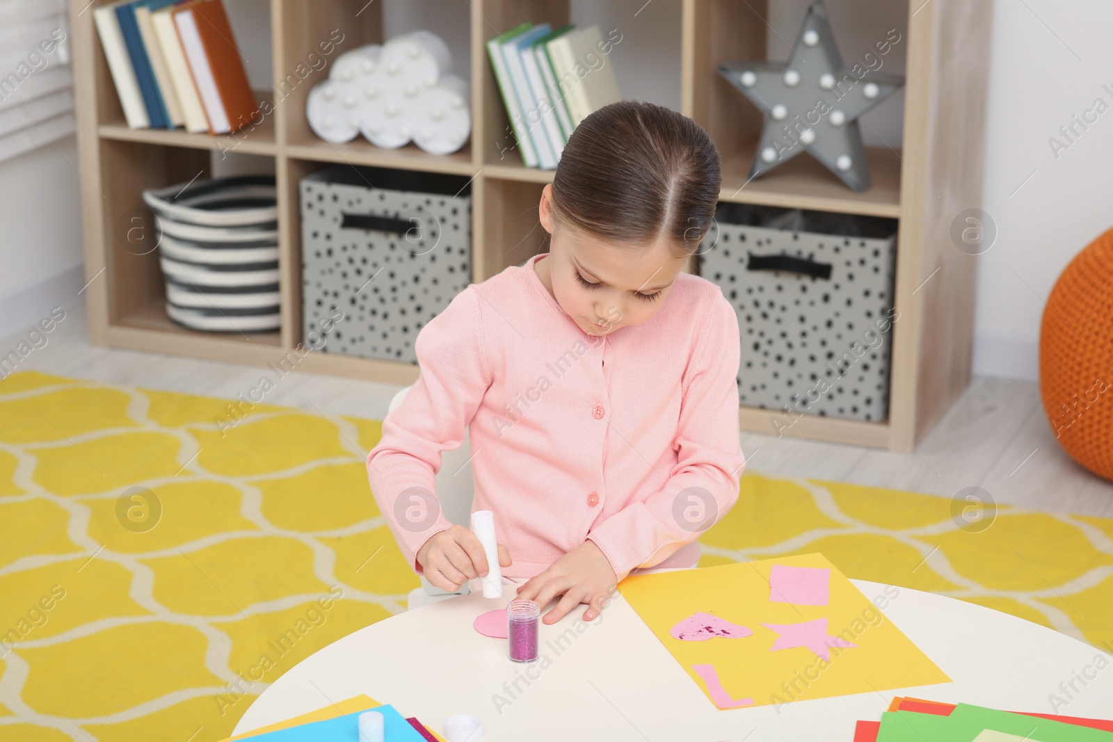 Photo of Cute little girl using glue stick at desk in room. Home workplace