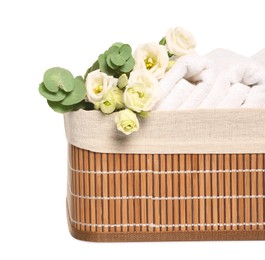 Photo of Wicker basket with folded soft terry towels, flowers and eucalyptus branch on white background