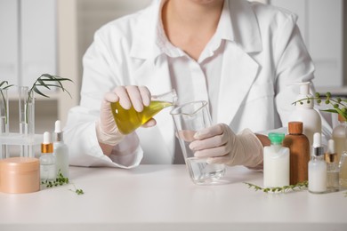 Photo of Dermatologist developing cosmetic product at white table indoors, closeup