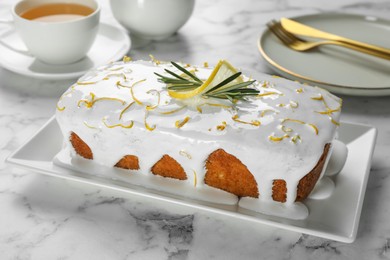 Photo of Tasty lemon cake with glaze and rosemary on white marble table