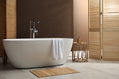 Photo of Modern ceramic bathtub and small table near brown wall in room