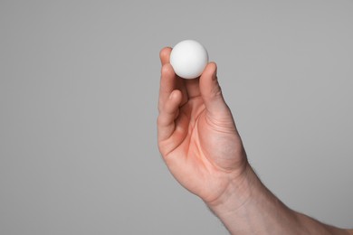 Photo of Man with ping pong ball on light grey background, closeup. Space for text