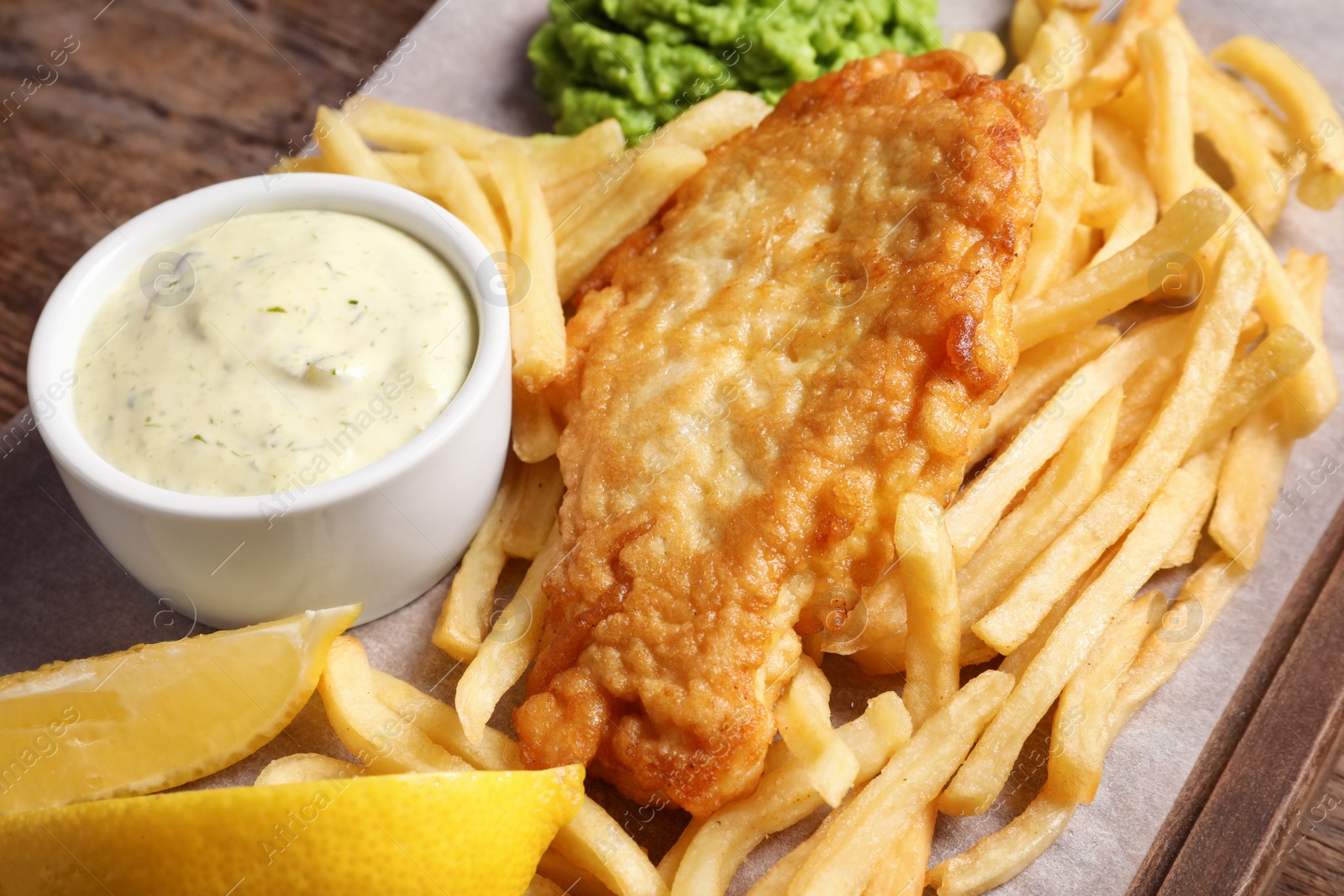 Photo of British traditional fish and potato chips on wooden board, closeup