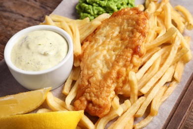 Photo of British traditional fish and potato chips on wooden board, closeup