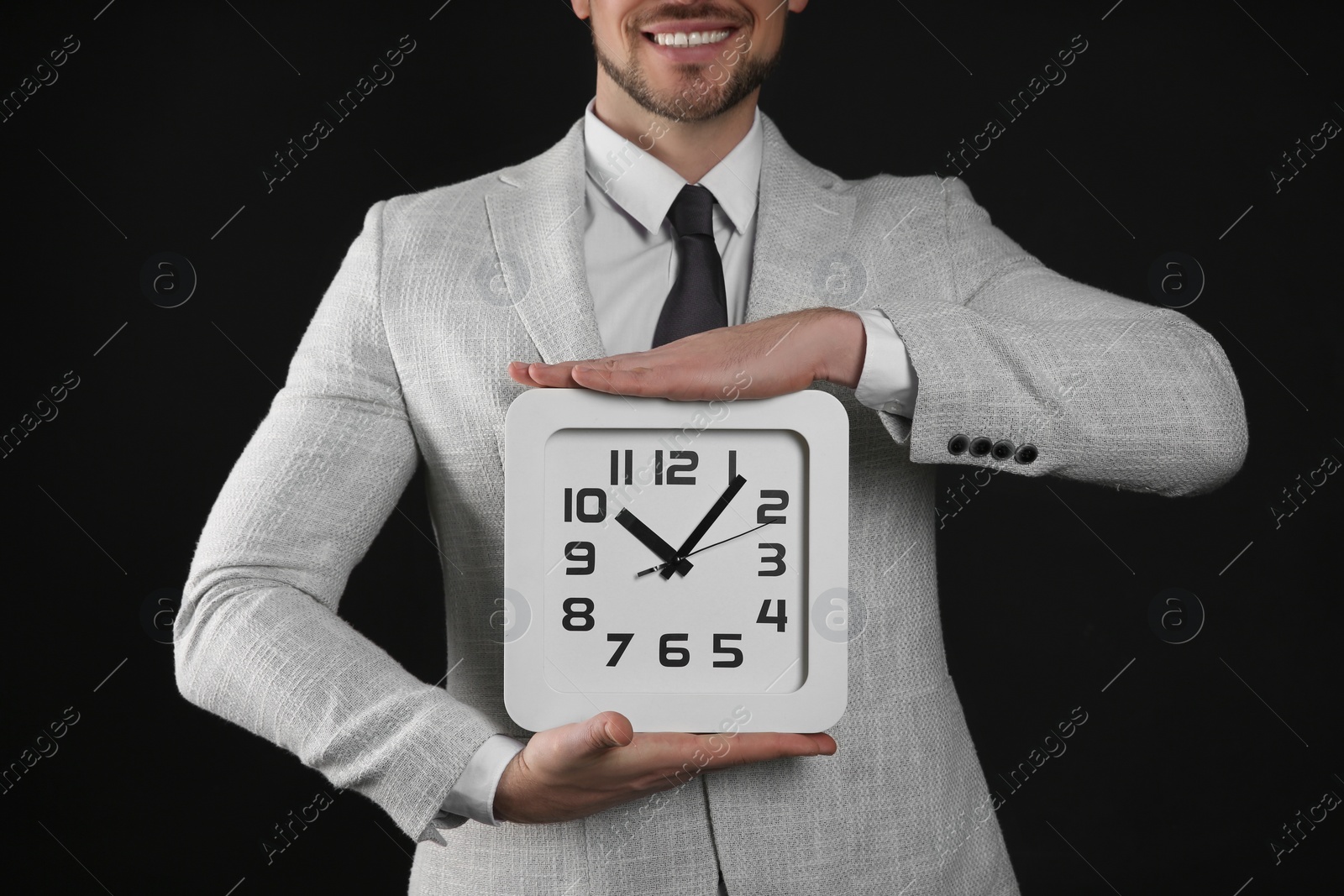 Photo of Happy businessman holding clock on black background, closeup. Time management