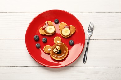 Photo of Creative serving for kids. Plate with cute bears made of pancakes, berries, banana and chocolate paste on white wooden table, flat lay