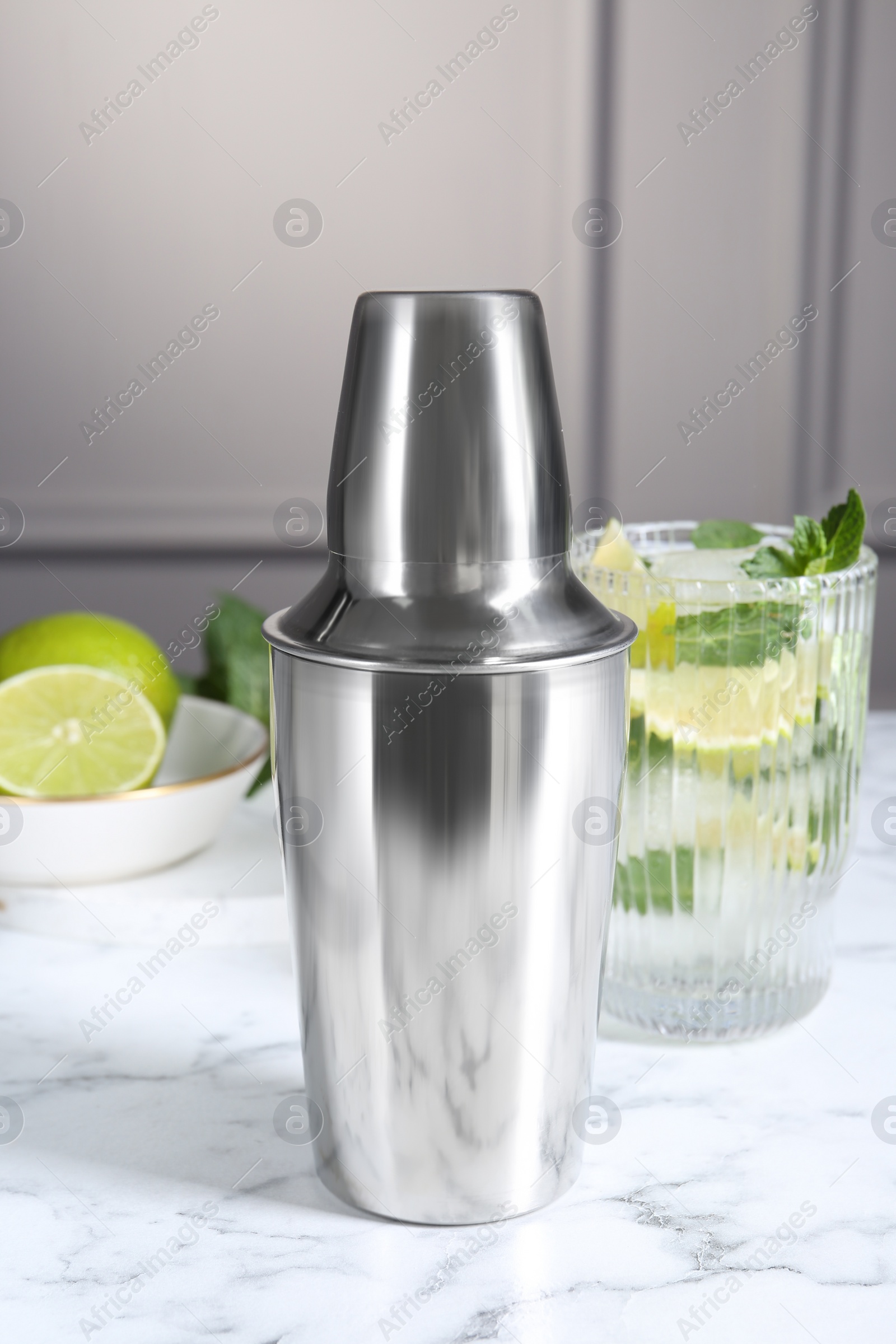 Photo of Metal cocktail shaker, delicious mojito, limes and mint on white marble table