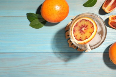 Photo of Delicious refreshing drink with sicilian orange, fresh fruits and leaves on light blue wooden table, flat lay. Space for text
