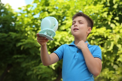 Little boy enjoying air flow from portable fan outdoors. Summer heat