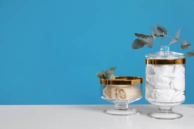 Photo of Jars with cotton pads and luffa sponges on white table against blue background. Space for text