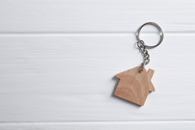 Photo of One keychain in shape of house on white wooden table, top view. Space for text