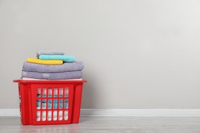 Photo of Laundry basket with clean towels on floor near light wall. Space for text